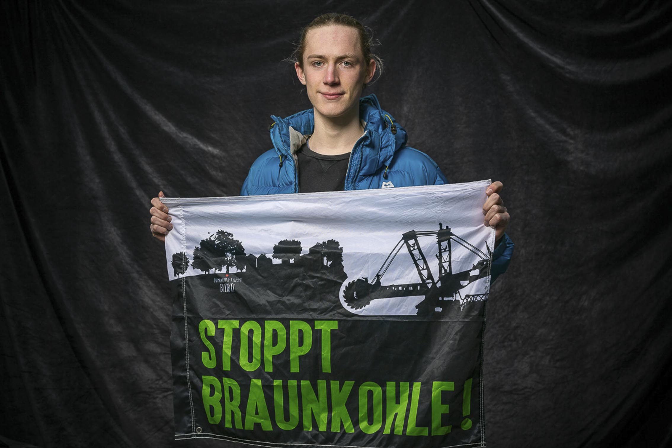 Student mit Banner Stoppt Braunkohle, vor Studiohintergrund auf einer FfF Demo in Köln