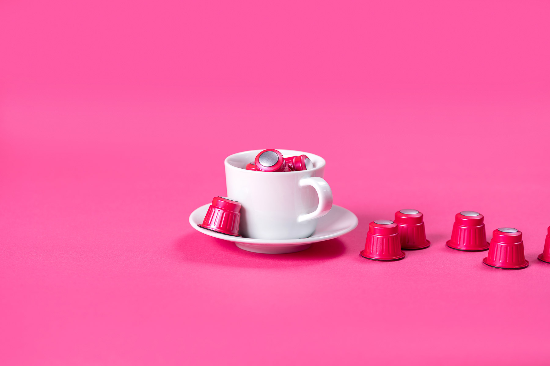 Rote Kaffekapseln in einer Kaffee-Tasse fotografiert, in einer pinken Umgebung.