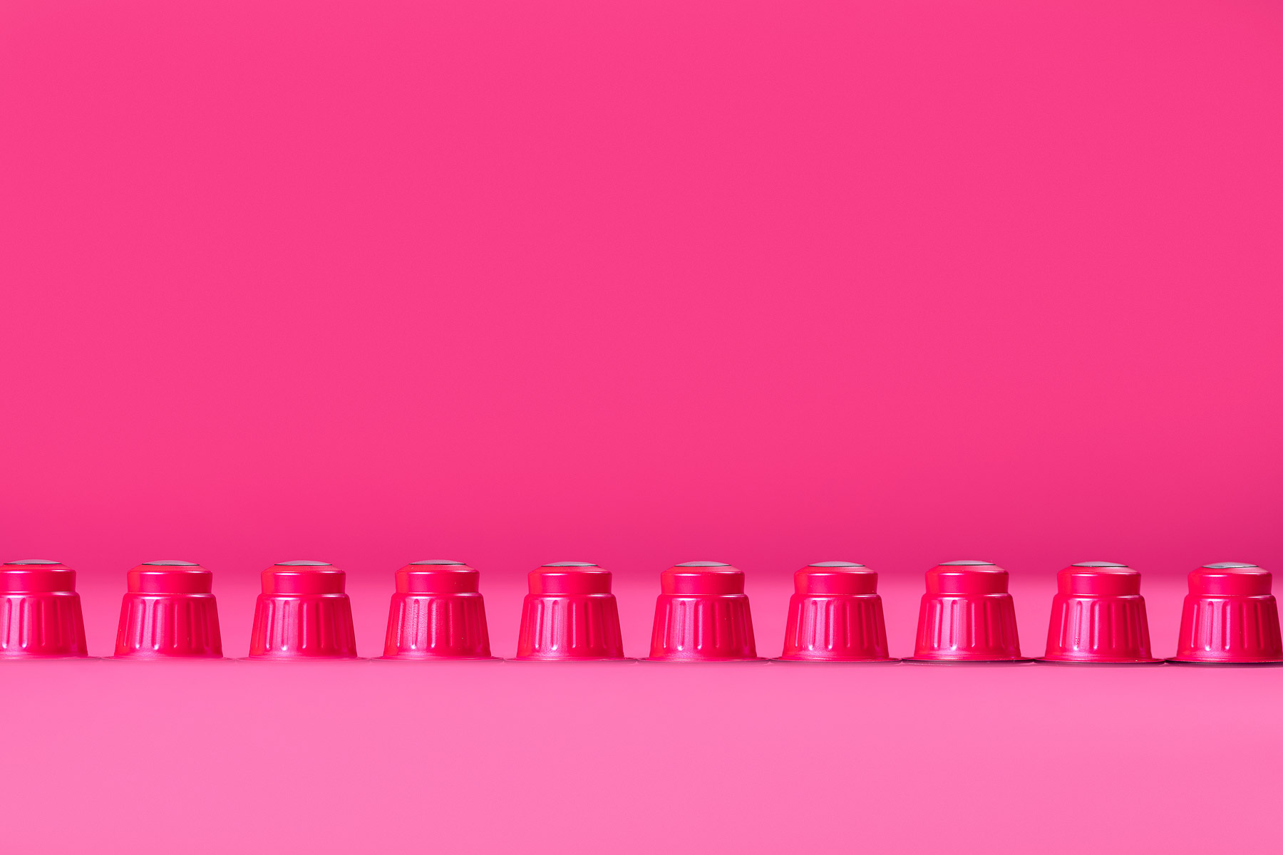 Rote Kaffekapseln in einer Reihe fotografiert, in einer pinken Umgebung.