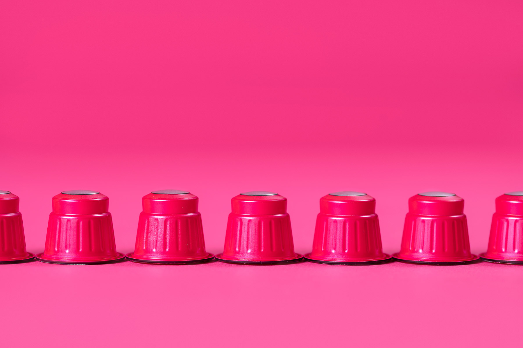 Rote Kaffekapseln in einer Reihe fotografiert, in einer pinken Umgebung.
