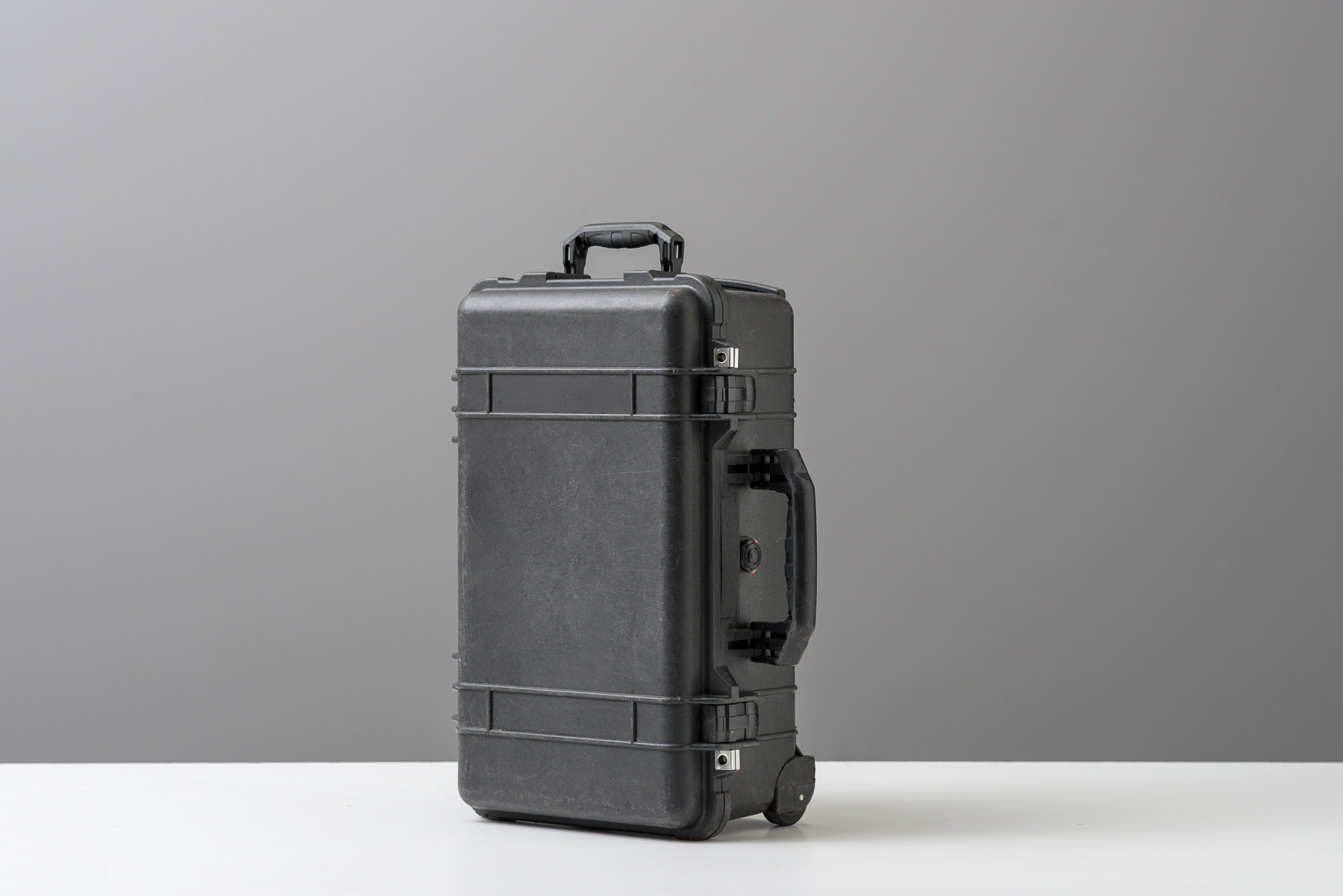 Pel-, Foto Koffer auf weißem Boden, vor grauem Hintergrund.